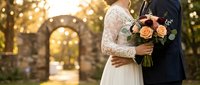 Bride and groom embracing with autumn bouquet during golden hour wedding ceremony with warm bokeh lights creating romantic atmosphere for celebration.