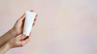 Female hand holding blank white cosmetic tube against neutral beige background for skincare, lotion, cream, or sunscreen product packaging mockup.