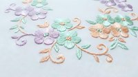 Delicate pastel embroidered flowers with swirling vines on white fabric. Soft pink, mint green, lavender blooms create elegant floral design for crafting projects.