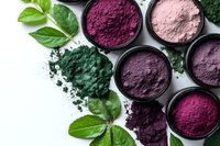 Natural pigment powders in shades of purple, pink and green with fresh green leaves on white background, organic dye ingredients for cosmetics and food coloring.