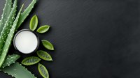 Fresh aloe vera leaves and natural cream in black bowl on dark slate background with green leaves, top view composition for spa and skincare concept.