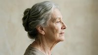 Senior Caucasian woman with gray hair in bun, profile view showing wrinkles and aging gracefully. Elderly female portrait for healthcare concepts.