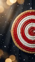 Handwoven wicker basket with red and white spiral pattern against dark background with golden bokeh lights and falling snow for festive decor.