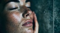 Young Asian woman with freckles and closed eyes in dramatic moody lighting against dark background, water drops and condensation creating atmospheric effect.