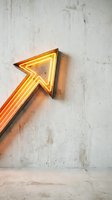 Glowing neon arrow sign pointing upward on weathered concrete wall, creating modern urban aesthetic for interior design and contemporary decor projects.