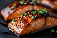 Glazed salmon fillet with teriyaki sauce, sesame seeds and chopped green onions on dark background, close up view of grilled fish with Asian marinade.