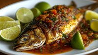 Grilled whole fish with herbs and lime wedges on white plate, seasoned with spices and fresh garnish for culinary and restaurant menu use.