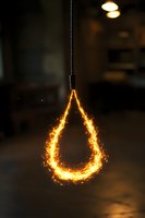 Glowing teardrop-shaped light fixture with sparkling fire effect creates dramatic ambiance against dark background, suspended from black cord. Artistic lighting design.