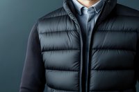 Stylish man wearing black puffer vest over blue shirt against dark background, modern casual business attire for cold weather.