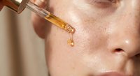 Golden facial serum drops from glass dropper onto glowing skin for anti-aging skincare routine and luxury beauty treatment regimen.