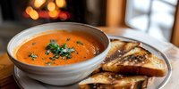 Creamy tomato soup garnished with fresh herbs served in a white bowl alongside toasted bread slices, perfect for food photography, restaurant menus, and culinary content.