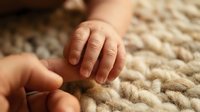 Tender moment of adult hand gently holding newborn baby hand on soft knitted blanket. Parenting, family bonding, care and protection concept.