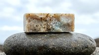 Handmade soap bar with natural ingredients resting on smooth stone, showcasing organic skincare and wellness products for cosmetic, beauty, and spa industry marketing.