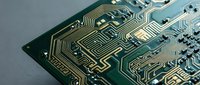 Close-up of a green printed circuit board with gold conductive traces and microchips, showcasing modern electronics technology and engineering.
