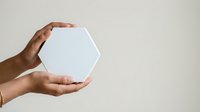 Male hand with medium skin tone holding white hexagonal shape against neutral background for product display and branding mockup purposes.