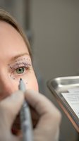 Young Caucasian woman receiving cosmetic eyelid surgery with surgical markings around eye area. Medical professional performing blepharoplasty procedure in clinic.