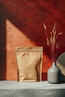 Kraft paper stand up pouch and ceramic vase with wheat stalks against terracotta wall with dramatic shadow play, minimalist modern composition on concrete shelf.