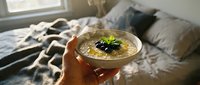 Creamy hummus dip with olive oil and fresh herbs held in hand over cozy bedroom setting, perfect for food styling and lifestyle content.