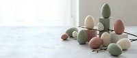 Pastel colored Easter eggs in soft green, pink and cream tones arranged with natural twigs on white surface near bright window for spring holiday decor.