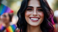 Young Hispanic woman with bright smile and dark wavy hair with purple highlights at pride celebration, showing genuine joy and acceptance against rainbow flag background.