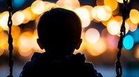Silhouette of child on swing against blurred bokeh lights creating magical evening atmosphere.