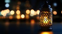 Decorative oriental lantern with glowing warm light inside against blurred bokeh background creating magical evening atmosphere.