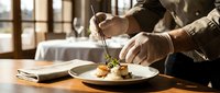Chef plating gourmet dish with tweezers in upscale restaurant kitchen, garnishing fine dining food with precision and care for culinary presentation.