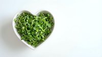 Fresh green arugula leaves in white heart-shaped bowl on clean background, healthy eating concept for salads and organic cooking recipes.
