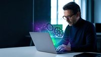 Middle-aged Caucasian businessman with glasses working on laptop with digital holographic interface displaying gears and technology elements in modern office.