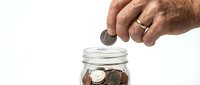 Close-up of male hand dropping coin into glass jar filled with savings, isolated on white background for financial planning and investment concepts.
