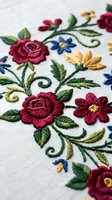 Colorful floral embroidery with roses and decorative stitching on white fabric showcasing traditional needlework craftsmanship and textile art techniques.
