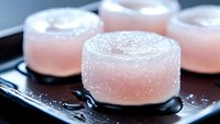 Pink translucent sugar coated jelly candies arranged on dark plate with reflective surface. Soft focus macro photography highlights crystalline texture and delicate details.