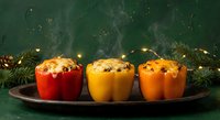 Three colorful stuffed bell peppers with rice and vegetables on dark plate, festive holiday dinner with pine branches and warm lights background.
