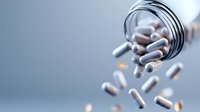 White capsule pills spilling from overturned glass bottle on blue background, representing medication, healthcare, pharmaceuticals, and wellness supplements for medical and health-related design projects.