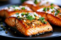 Grilled salmon fillets glazed with honey and soy sauce, garnished with fresh herbs and black sesame seeds on dark plate, close up view of juicy fish steaks.
