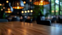 Atmospheric restaurant interior with warm pendant lights casting golden glow over empty wooden table. Blurred bokeh background creates cozy evening ambiance.