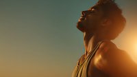Silhouette of athletic Black man in tank top looking up at sunset, golden light illuminating his profile against teal sky background.