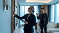 Professional female real estate agent showing luxury apartment to potential male buyer in modern high-rise building with city views and contemporary interior design.