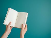 Open book with blank pages held by hands against turquoise background, suitable for publishing, education, and creative writing projects.