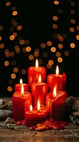 Red candles burning with warm flames on rustic wooden surface against dark background with golden bokeh lights creating festive holiday atmosphere.