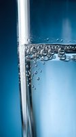 Close-up macro shot of sparkling water bubbles rising inside a clear glass against a deep blue background, capturing purity and refreshment.