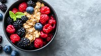 Fresh mixed berries and granola in dark bowl on gray concrete background, healthy breakfast with raspberries, blackberries, blueberries and oats flakes.