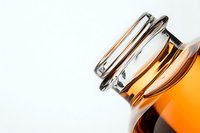 Amber glass bottle with metal clasp lid photographed at creative angle on white background, showing minimalist composition and liquid contents.