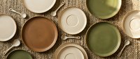Overhead view of assorted ceramic bowls and saucers in neutral and sage tones arranged on natural linen fabric, suitable for tableware, kitchenware, and home decor design projects.