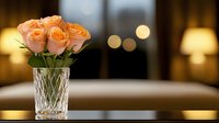 Peach roses in crystal vase against soft bokeh background with warm evening lights creating romantic atmosphere. Elegant floral arrangement for special occasions.