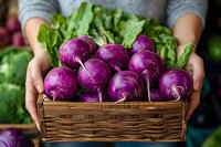 Fresh purple kohlrabi bulbs in woven basket held by farmer hands against dark background with green leaves, organic harvest from local garden.