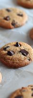 Fresh baked chocolate chip cookie with melted dark chocolate chunks on parchment paper, close-up macro shot showing soft, chewy texture and golden brown surface.