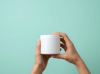 Hands holding white cosmetic jar with peach lid against turquoise background for skincare, beauty product packaging, and cosmetics branding mockup.