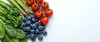 Fresh organic vegetables and berries arranged on white background including asparagus, cherry tomatoes, spinach and blueberries for healthy eating.