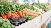 Fresh organic vegetables displayed in wooden crates at farmers market including carrots, eggplants, bell peppers and leafy greens. Local produce arrangement.